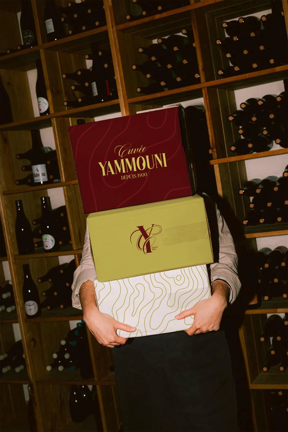 Person holding burgundy and yellow Cuvée Yammouni wine packaging